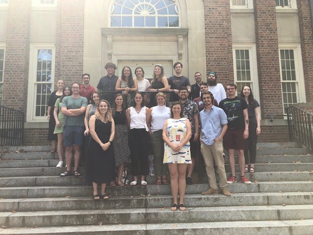 22 graduate students stand on the steps outside of Murphey Hall.